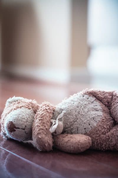 Forlorn old worn teddy bear left in empty room